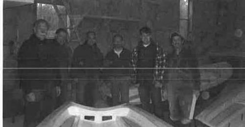 A group of volunteers posing beside a refurbished Albacore hull in the Shelburne boat shop