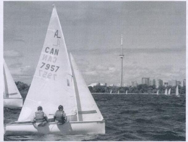 An Albacore, sail number CAN 7957, sailing with two crew with the Toronto skyline in the distance