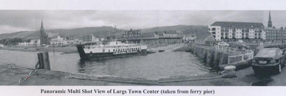 A panoramic multi-shot photo of Largs town centre and harbour, taken from the ferry pier, showing a ferry docked and the town's waterfront buildings
