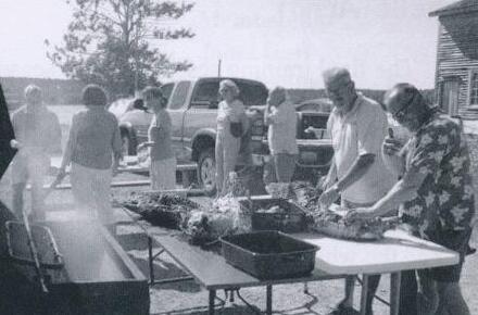 Volunteers preparing a pig roast outdoors on folding tables