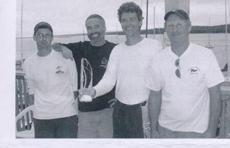 Four men posing together at the yacht club, one holding a trophy
