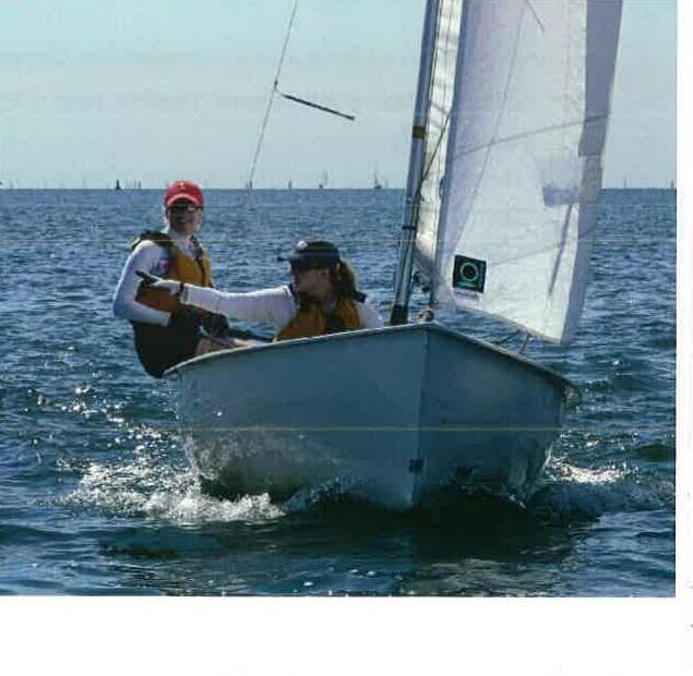 Two young sailors in an Albacore, one coaching the other at the helm