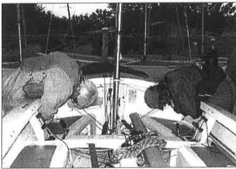 Two people leaning over the gunwales tightening side tank fasteners