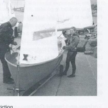Barney Harris adjusting the rigging of an Albacore on the beach while a young crew member looks on
