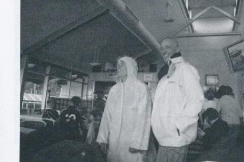 Two people in white sailing jackets standing inside a busy clubhouse, one asking "Mary, care to explain?"