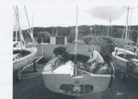 Two sailors rigging an Albacore in a boatyard among other trailered dinghies