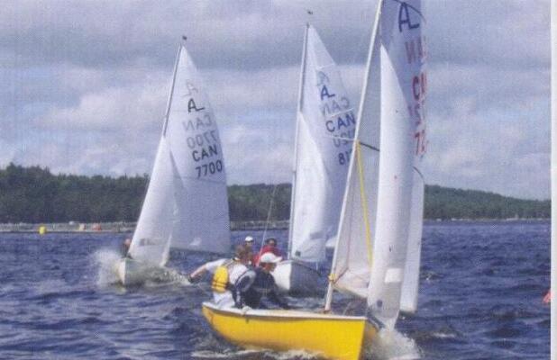 Three Albacores sailing close together, a yellow-hulled boat in front