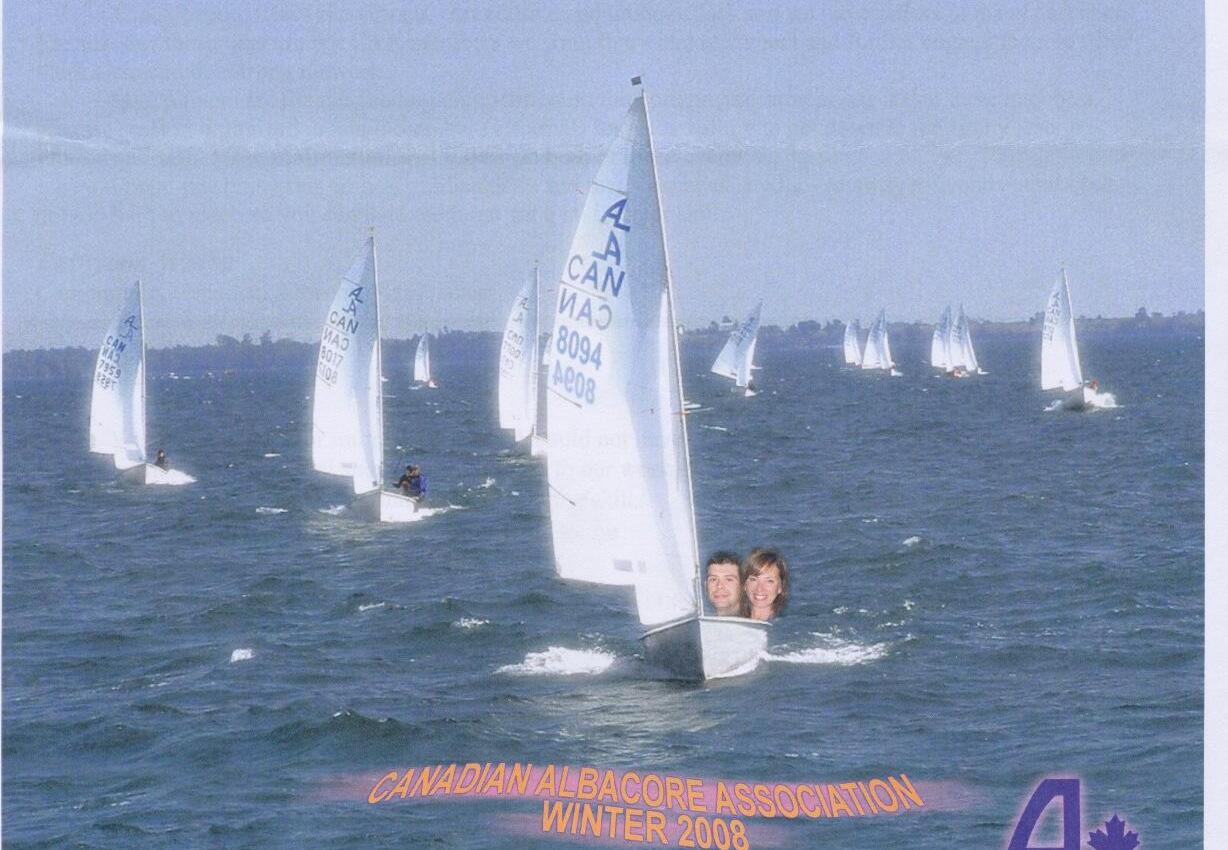 A fleet of Albacores sailing upwind, with a joke composite of two people's faces poking out of the lead boat's cockpit as if swimming alongside it