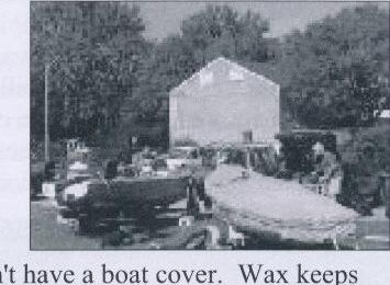 An Albacore hull stored outdoors beside a shed, partially covered, with another boat nearby