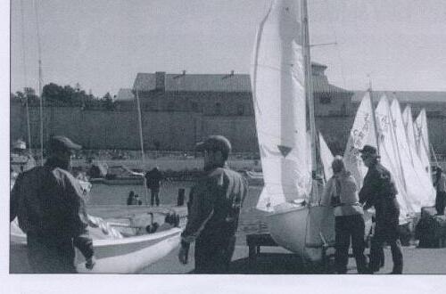 Sailors rigging boats in a boat park with a stone fortress wall behind