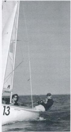 A crew launching Albacore number 13 from a beach, one sailor at the tiller and one seated forward