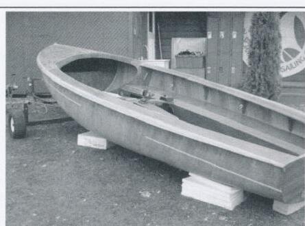 An unpainted wooden Albacore hull upside down on a trailer in a driveway