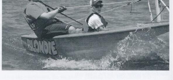 An Albacore named Blondie planing hard with helm and crew hiking out, spray flying from the transom