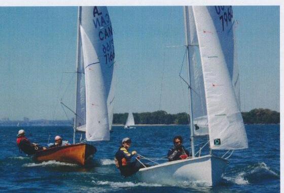 Two Albacores racing close together on a harbour with a city skyline in the distance