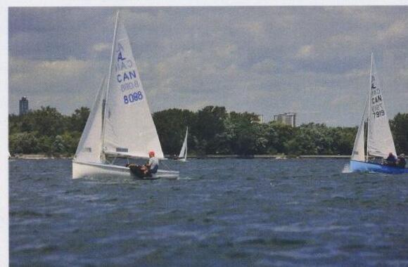 Two Albacores sailing separately on open water with a city skyline behind