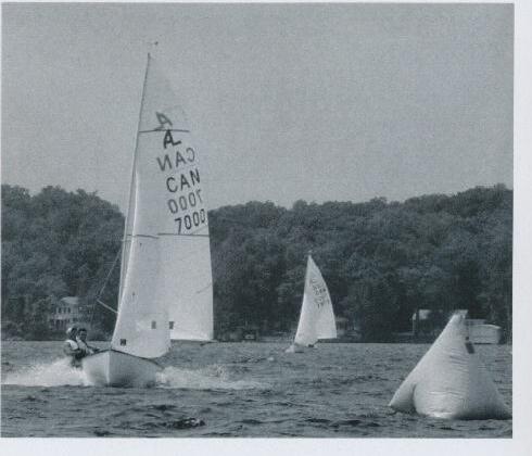 An Albacore sailing hard with CAN 7000 on its sail, two more boats trailing behind