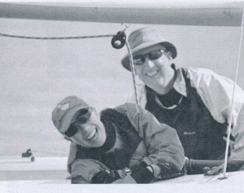 Two sailors laughing together on an Albacore, one wearing a bucket hat and sunglasses