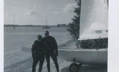 Two people in drysuits standing beside a trailered Albacore on a beach