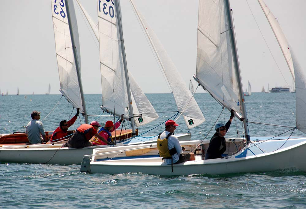 Two Albacores close together at a start line, crews hiking out with the fleet and a ferry in the background