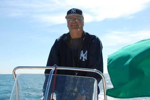 Peter Vasoff wearing a New York cap, standing at the helm of a boat