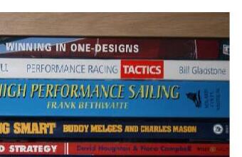 A stack of sailing book spines: Winning in One-Designs, North U Performance Racing Tactics, High Performance Sailing, Sailing Smart, and Wind Strategy