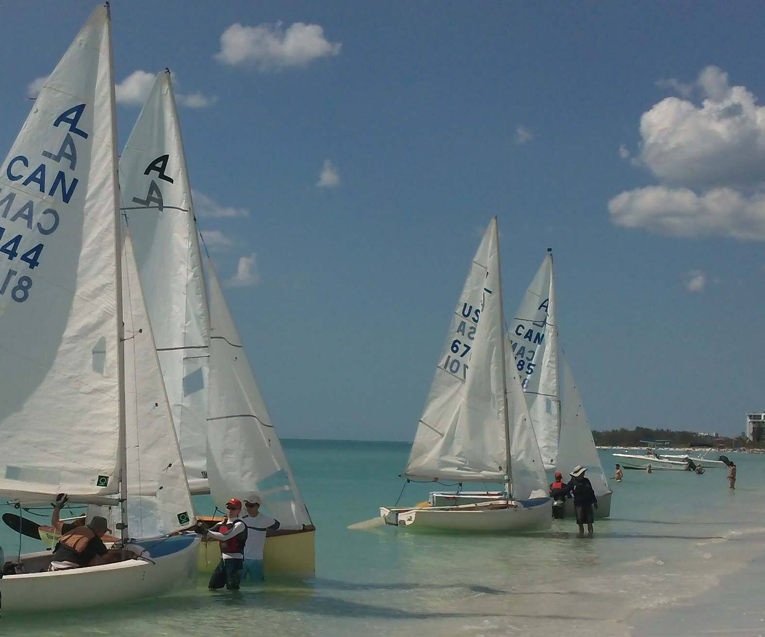 A start of Albacores launching off a Sarasota beach, sails against blue sky