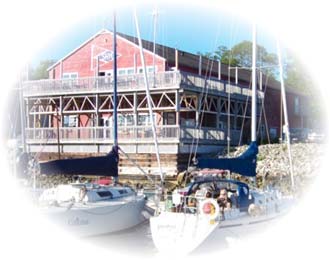 A red boathouse with sailboats docked alongside