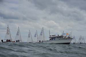 A fleet of Albacores starting near a committee boat in grey conditions