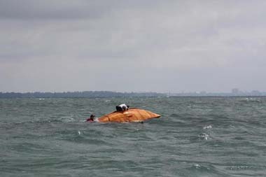 A capsized orange-hulled dinghy with a swimmer alongside