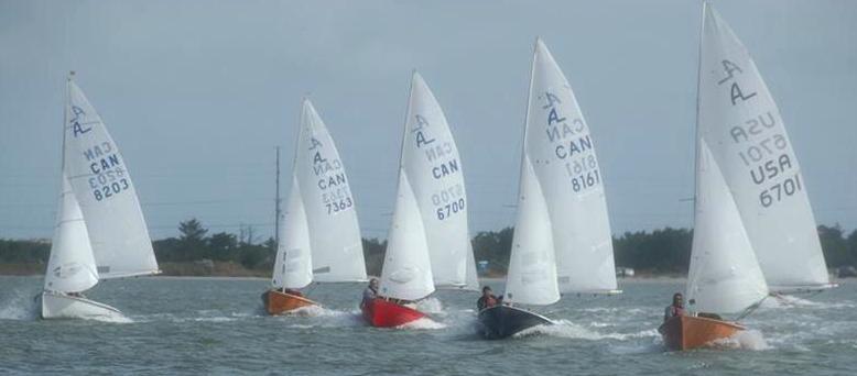 A colourful fleet of Albacores reaching, several with red, black, and orange hulls