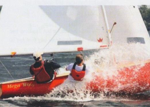 Crew hiking hard on a red Albacore named Mega Woof, spray off the bow