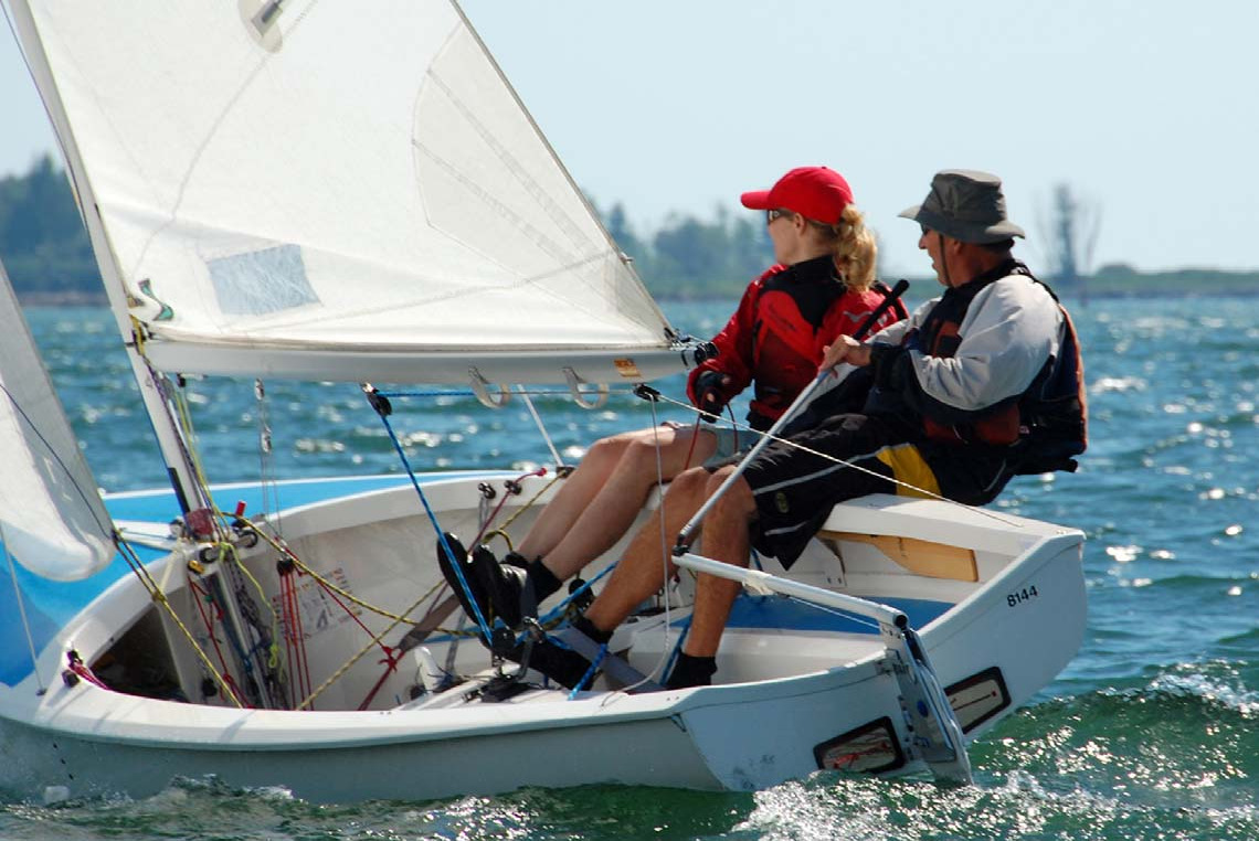 A crew hiking out hard on Albacore 8144 under sail, spray coming off the bow