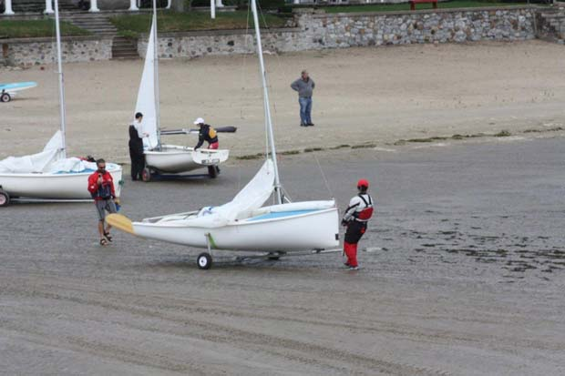 Sailors trailering Albacores across a beach launch, one crew in bright red gear