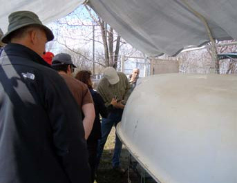 Members gathered under a tent measuring a hull at CAA Day