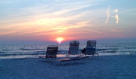 Three beach chairs facing a sunset over the Gulf of Mexico