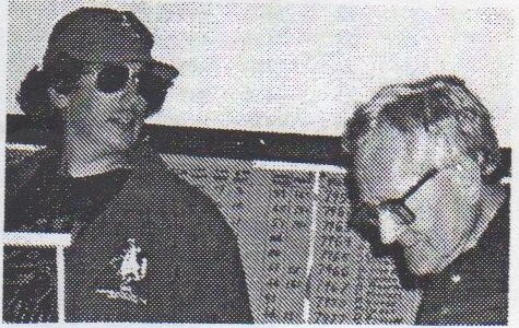 Barry Farrell in a cap and sunglasses beside OHCC Commodore John Ashby, in front of the results board