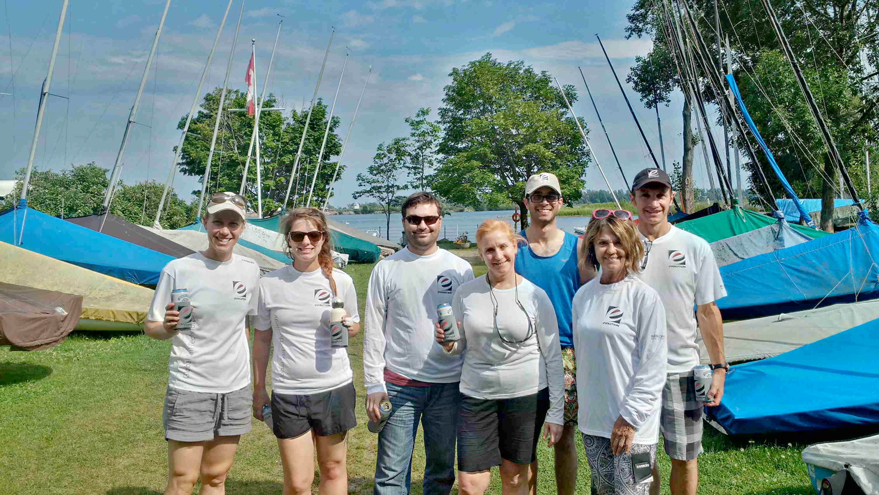 Seven clinic participants in matching Evolution Sails shirts posing in front of rigged Albacores