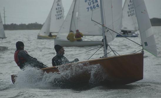 An orange-hulled Albacore planing hard with spray flying, crew hiked out on a reach