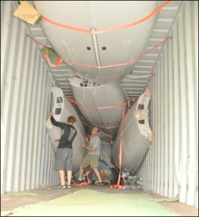 Two men wrestling an Albacore hull into position inside a shipping container packed with strapped hulls