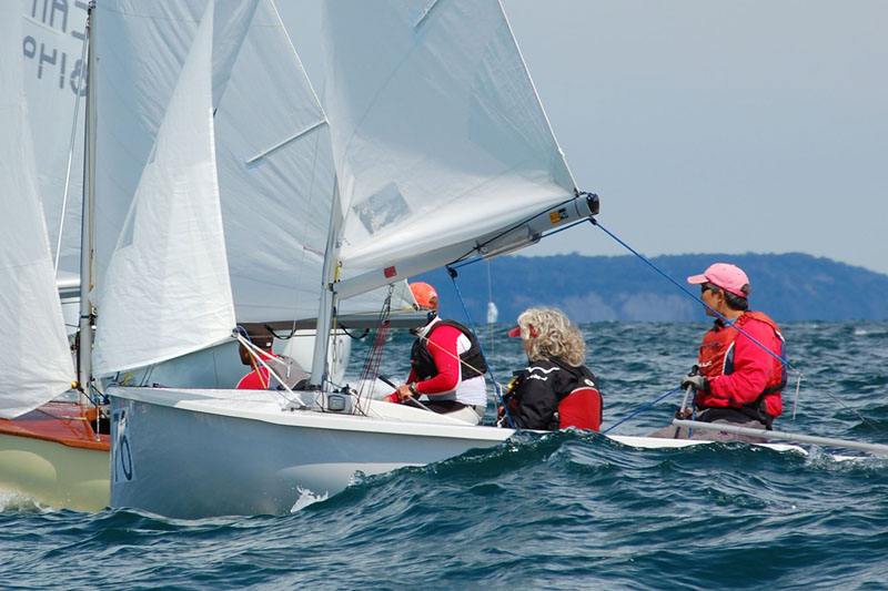 A close-up of an Albacore crew gybing near another boat