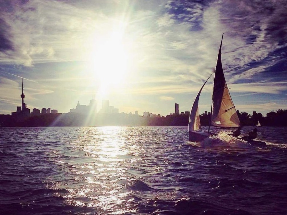 An Albacore sailing into the sun with the Toronto skyline silhouetted