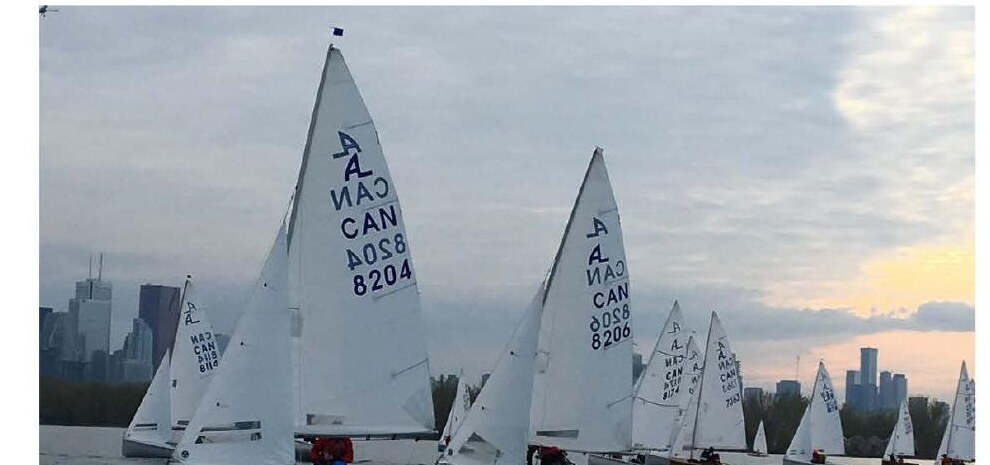 Albacore fleet sailing at dusk with the Toronto skyline behind