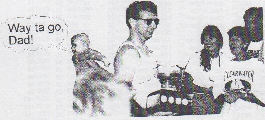 Bruce Withrow holding a trophy beside a baby with a speech bubble reading “Way ta go, Dad!”, with Sandy Swiatlowski in a Clearwater shirt and others laughing