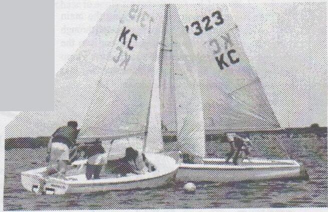 Two Albacores, one with sail number 323, overlapped at a round mark buoy, appearing to round it in opposite directions