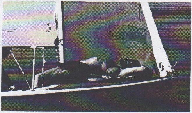 An Albacore skipper lying flat on his back along the side deck under the sails, grinning