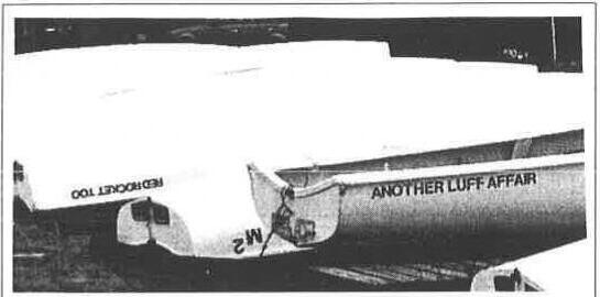 Albacores stored on a rack; the transom of one reads “Another Luff Affair” and another “Red Rocket Too”