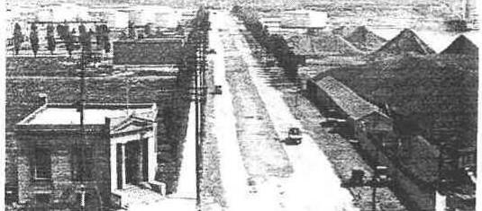 Archival photo looking down Cherry Street in the 1920s, with a columned bank building, utility poles and industrial sheds