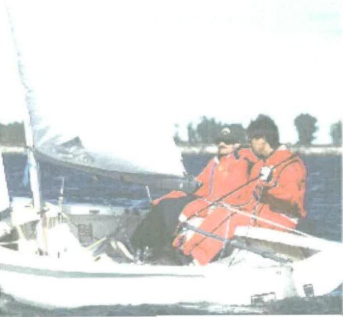 Two sailors in orange foul-weather gear sailing an Albacore close-hauled