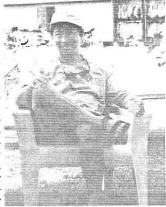 A young man in a cap and windbreaker seated in a chair, holding a bag on his lap