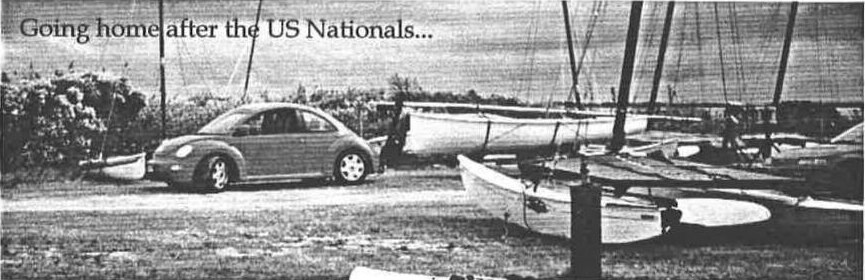 A Volkswagen Beetle parked beside Albacores on trailers in a dinghy park